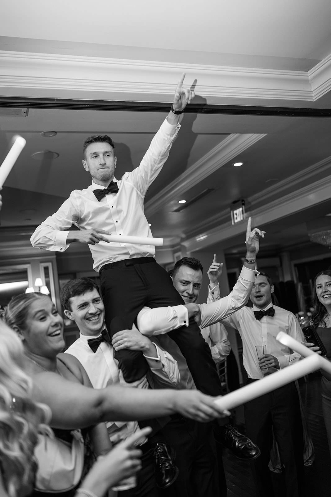 Black and white photo of the groom celebrating on guests' shoulders during a high-energy reception dance.